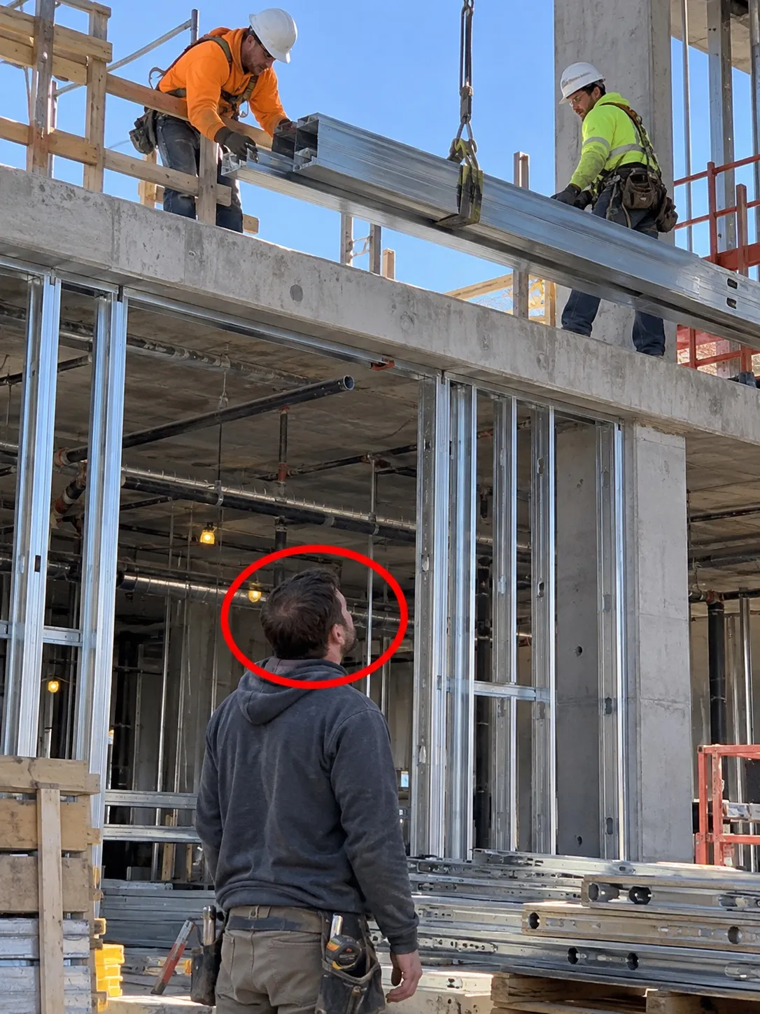 Site photo circled in red: ground-level worker beneath suspended steel beam without visible hard hat.